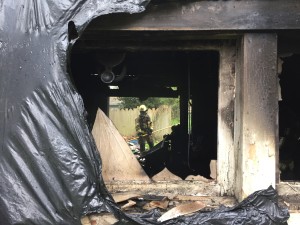 An NKF&R firefighter, visible through broken windows and doors, pauses from the hard work of digging through debris to snuff hotspots remaining after a fire of unknown origin destroyed a garage in Suquamish on Tuesday evening. 