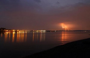 Kingston's port and ferry terminal are lit up across Apple Tree Cove as lightning strikes across Puget Sound.
